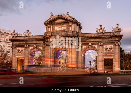 Puerta de Alcala monumento a Madrid durante il periodo natalizio al tramonto. Vista a lunga esposizione con percorsi semaforici Foto Stock