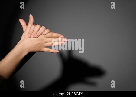 Donna che fa cane ombra con le mani su sfondo scuro Foto Stock