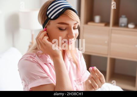 Giovane donna che inserisce i tappi per le orecchie in camera da letto Foto Stock