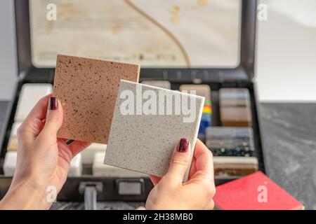 Campioni di materiale per il piano di lavoro. Le mani femminili stanno scegliendo gli elementi interni per la ristrutturazione. Campioni di pietra acrilica in mani. Foto Stock