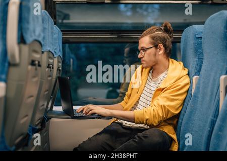 Giovane adolescente con occhiali viaggia in treno con un computer portatile. Foto Stock