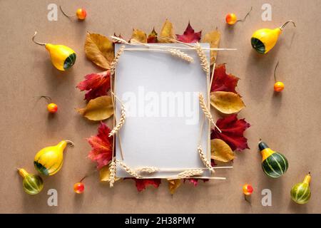 Cornice autunnale realizzata con foglie di autunno naturale, spighe di grano e zucche decorative e bacche. Spazio per la copia, posizione del testo sulla pagina di carta bianca. Naturale Foto Stock