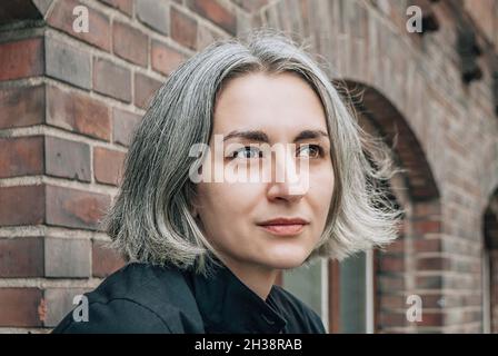 La donna dai capelli grigi guarda via sul retro dell'edificio in mattoni Foto Stock
