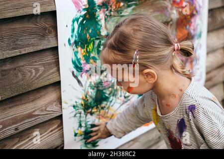 Bella ragazza pittura con colori colorati con una spazzola nel cortile con volto sporco e vestiti. Foto Stock