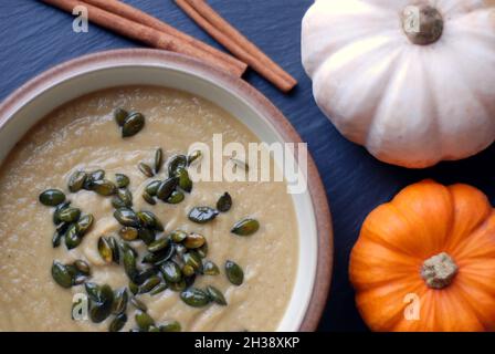 Zuppa di zucca in una ciotola con zucche e barrette di cannella accanto su sfondo nero. Foto Stock