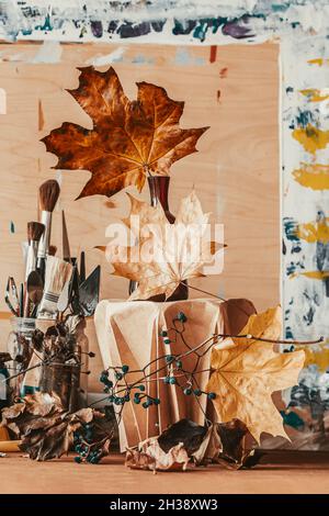 La natura morta con pennelli artistici, foglie autunnali, tavolozza dell'artista e cornice fotografica. Atmosfera e ispirazione autunnali Foto Stock