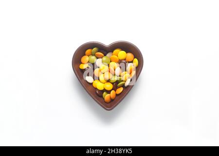 caramelle dolci multicolore in ciotola a forma di cuore su sfondo bianco, vista dall'alto. Spazio per il testo Foto Stock