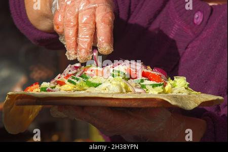 Produzione di involucri freschi in una stalla del mercato agricolo. Le mani delle donne che preparano una confezione per un cliente in un mercato di Street food. Foto Stock