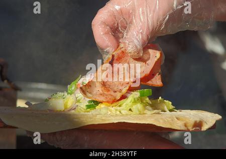 Produzione di involucri freschi in una stalla del mercato agricolo. Le mani delle donne che preparano una confezione per un cliente in un mercato di Street food. Foto Stock