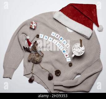 Cappello santa rosso con maglione di Natale lavorato a maglia paraphernalia con l'iscrizione buon natale su sfondo bianco. Foto Stock