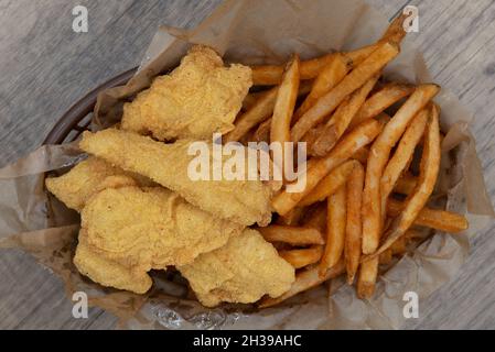 Vista dall'alto di un invitante cestino di bastoncini di pesce impanato croccante e un generoso servizio di patatine fritte in un cestino. Foto Stock