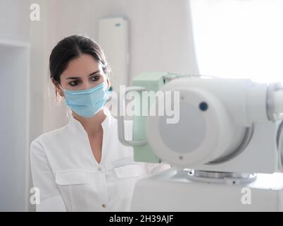 Clinic Radiology Room: Bella donna multietnica regolazione X-Ray Machine in ospedale moderno. Tecnico in reparto radiologia accendere scanner Foto Stock