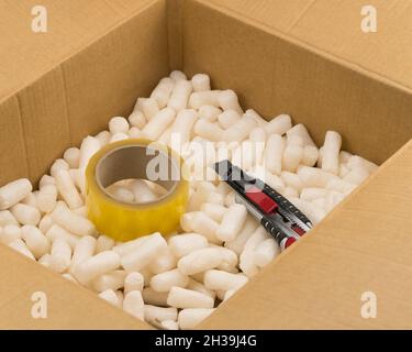 Scatola di cartone con stucco in polistirolo per un imballaggio sicuro. Coltello per cancelleria e nastro interno Foto Stock