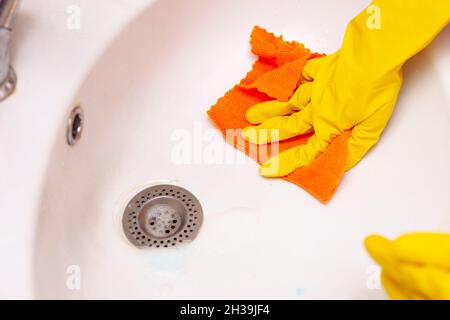 mano in un guanto di gomma giallo pulisce il lavandino in bagno Foto Stock