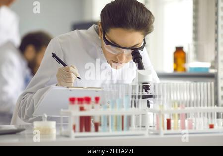 Donna in un cappotto bianco guarda al microscopio. Foto Stock