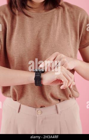 Immagine ravvicinata della giovane donna che punta allo schermo dello smartwatch durante il controllo delle notifiche Foto Stock