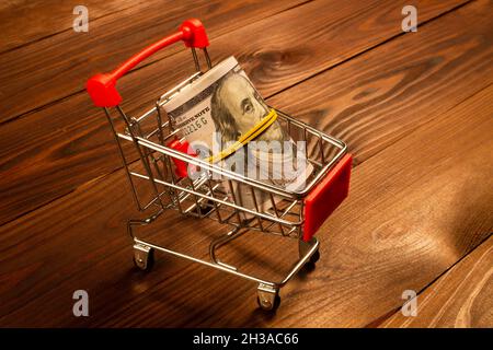 Concetto di Black Friday. WAD di denaro nel carrello. Dollari USA in un piccolo carrello in metallo su uno sfondo di legno marrone bello. Pronto Foto Stock