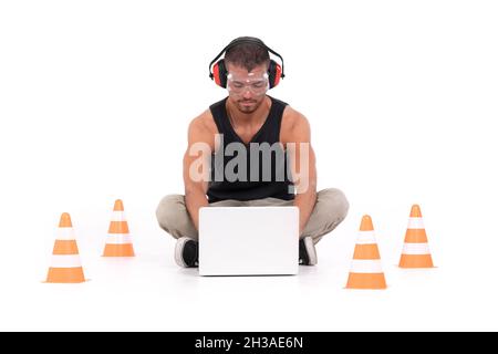 Costruttore che lavora con un laptop in un'area delimitata con coni arancioni Foto Stock