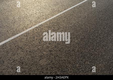 La texture di una nuova strada asfaltata con una striscia bianca divisoria in una mattinata di sole Foto Stock