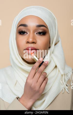giovane donna musulmana in hijab applicazione rossetto isolato su beige Foto Stock