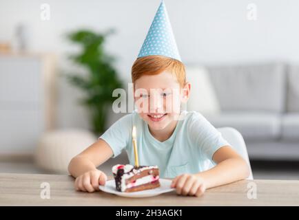 Ragazzo allegro che indossa il cappuccio di carta blu, celebrando il compleanno Foto Stock