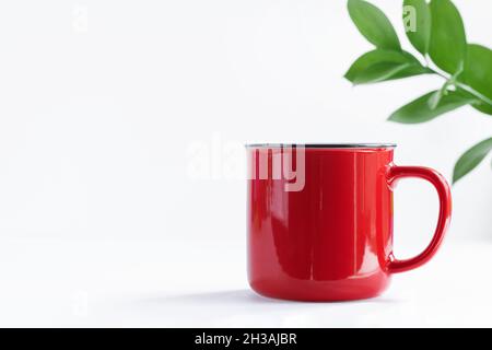 Tazza rossa con manico isolato su sfondo bianco con foglie. Foto Stock