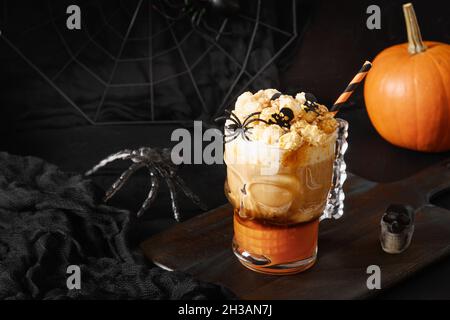 Halloween Pumpkin spice latte caffè con panna montata decorata teschi e popcorn in elegante galss su sfondo nero. Foto Stock