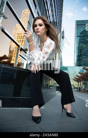 Giovane donna d'affari nella città moderna di skyscapers con capelli lisci lunghi Foto Stock