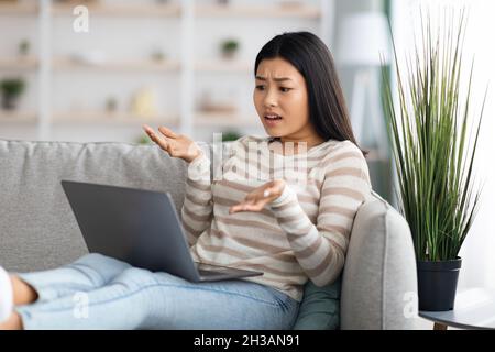 Confuso giovane donna asiatica che soffre problemi con il portatile a casa Foto Stock