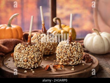 Mele al caramello ricoperte di noci su un piatto di legno con sfondo autunnale da una finestra Foto Stock