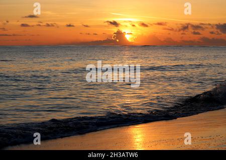 Tramonto su una spiaggia sabbiosa, il sole arancione splende attraverso le nuvole. Mare serale, sfondo per viaggi romantici Foto Stock