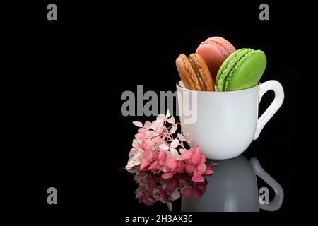 Un assortimento di amaretti in una tazza di porcellana bianca su sfondo nero con riflessi. Foto Stock