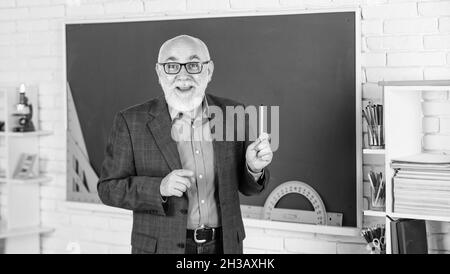 Insegnante maturo che gode di lavoro. Condivisione delle conoscenze. Più strumenti introdotti nelle aule di tutti i giorni. Insegnante senior alla lavagna. Torna a scuola Foto Stock