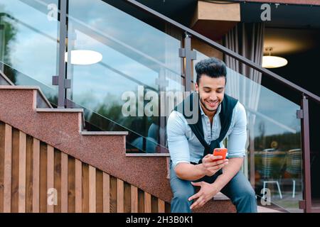 Attraente giovane uomo arabo in piedi con la valigia in mano e in posa per la macchina fotografica, mettere un piede prima dell'altro e si basa sulle scale vicino al Foto Stock