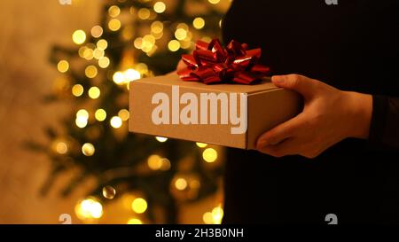 Le mani femminili danno una scatola del regalo di sorpresa sullo sfondo di decorazione dell'albero di Natale. Natale, Capodanno, concetto di compleanno. Foto Stock