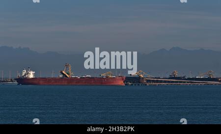 Portarinfuse Hyundai Atlantic caricando carbone a Roberts Bank Superport, parte del porto di Vancouver con le sagome delle montagne sullo sfondo. Foto Stock