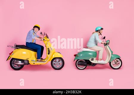 Foto lato profilo full size di shocked stupito coppia matura in casco bianco grigio capelli ride scooter veloce isolato su sfondo rosa Foto Stock