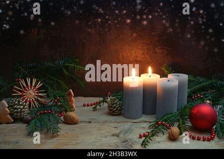 Secondo Avvento, due delle quattro candele sono accese, bauble rosso, stella paglia, rami di abete e decorazione di Natale su tavole di legno rustico contro un b scuro Foto Stock