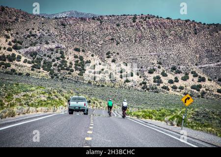 I ciclisti sono passati in camion su due Land Lonliest Highway in America attraverso il Nevada con montagne coperte di scrub sullo sfondo. Foto Stock