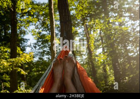 Foto POV di unghie della punta dipinte della donna in amaca in una foresta verde Foto Stock