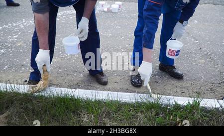 Persone che lavorano a mano indossando guanti bianchi e verniciate con una spazzola di vernice sui bordi. Clip. Lavoratori in forma dipinta Foto Stock