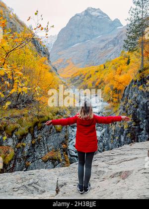 Autunno autunnale alberi e donna viaggiatore in giacca rossa. Paesaggio di montagna con fiume Foto Stock