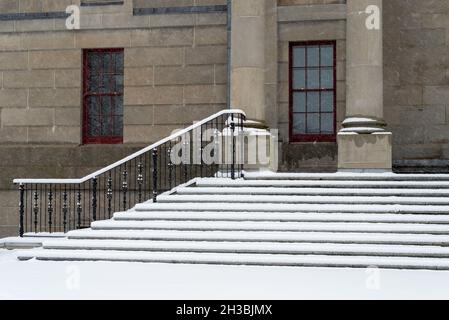 Grandi colonne rotonde in cemento in cima a gradini in marmo con binari in ferro nero per un edificio legale. L'edificio governativo ha una porta rossa alta. Foto Stock