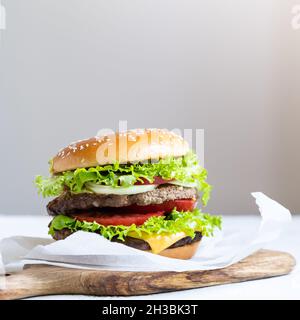 Cheeseburger doppio con cotolette di vitello, pomodori, foglie di lattuga e cetrioli. Fast food. Foto Stock