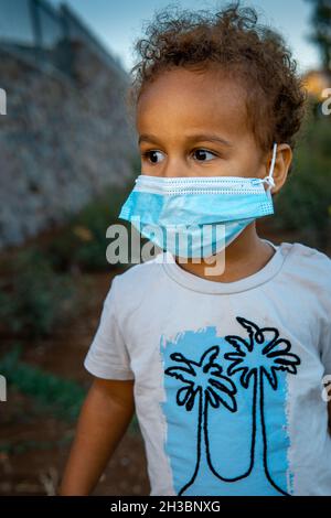 ritratto di etiope israeliano interrazziale toddler che indossa una maschera monouso corona cocid-19. cercando di continuare a lasciare il più normale possibile durante Foto Stock