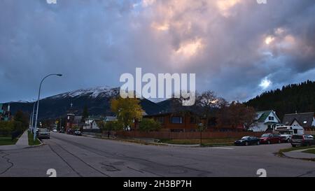 Scena tranquilla nella cittadina di Jasper nelle Montagne Rocciose canadesi con strade vuote, parcheggio auto e case in serata nuvolosa in autunno stagione. Foto Stock