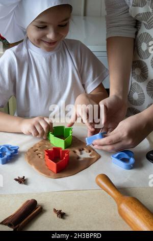 Felice madre e figlia che tagliano varie forme di biscotti in cucina. Mamma e figlia fanno biscotti di pan di zenzero a casa e Buon divertimento. Casa Foto Stock