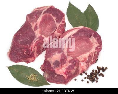 Due tagli crudi di carne al collo di maiale con pepe nero e foglie di alloro su sfondo bianco Foto Stock
