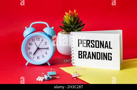 Testo DI BRANDING PERSONALE scritto su blocco note. Su una sveglia di sfondo rosso e giallo, cactus e clip di carta. Progetto di progettazione. Branding e marketing Foto Stock