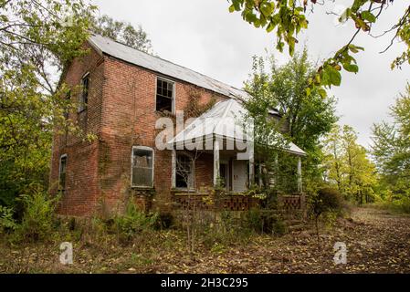 Una casa in mattoni abbandonata con un tetto di fianco sul portico nel Midwest degli Stati Uniti. Foto Stock